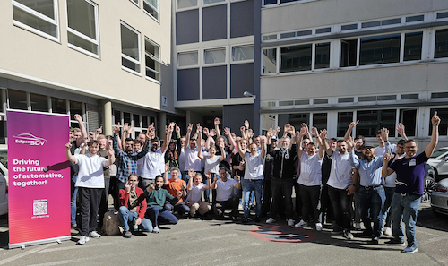 A group of people standing in front of a university building and next to an Eclipse banner, cheering