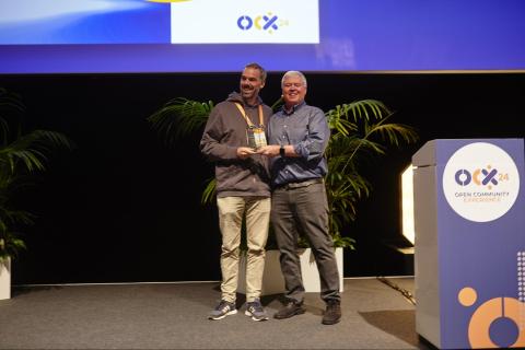 Two men standing close two each other on a stage, holding an award