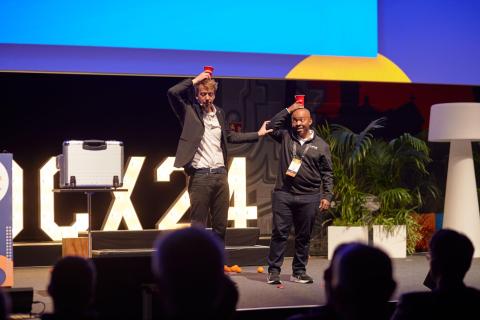 Two men balancing red cups on their heads on a stage