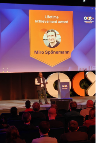 Award ceremony at Open Community Experience 2026, with a speaker on stage announcing the Lifetime Achievement Award for Miro Spönemann, displayed on a large screen.