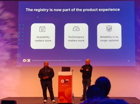 Gael Blondelle and Thabang Mashologu presenting on stage at Open Community for Tooling, with a slide explaining that the registry is now part of the product experience, highlighting availability, performance, and reliability as key priorities.